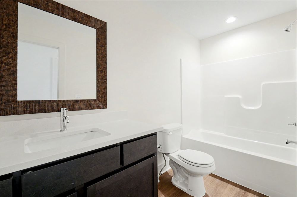 Cedar Crest duplex bathroom with a quartz-look vanity top, dark cabinet base, framed mirror and tub-shower – Wichita, KS