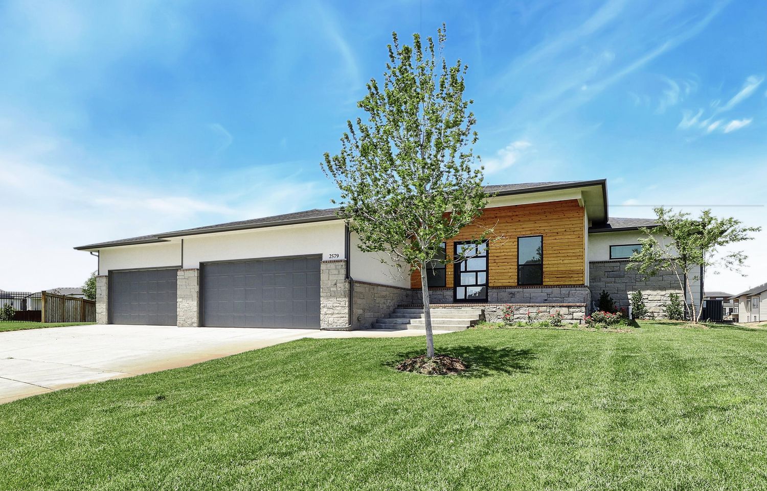 Front elevation of 2579 Doris Court — a walkout ranch with cut stone at the garage, cedar cladding across the entry gable and white siding above – Wichita, KS