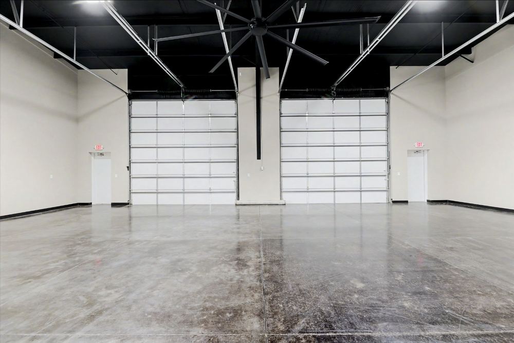 Interior of an Eagle Lux garage condo bay showing two tall white overhead doors and a large black ceiling fan – Maize, KS