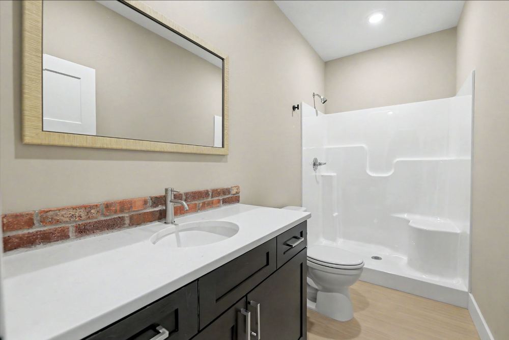 Eagle Lux garage condo loft bathroom with a quartz-look vanity, brick backsplash and walk-in shower – Maize, KS