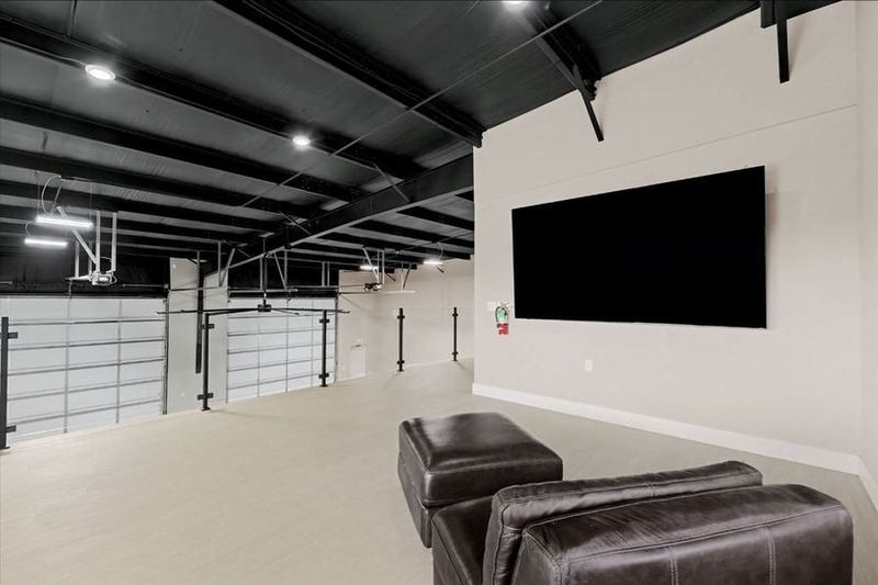 Eagle Lux garage condo mezzanine lounge with a wall-mounted screen and leather seating overlooking the door line – Maize, KS