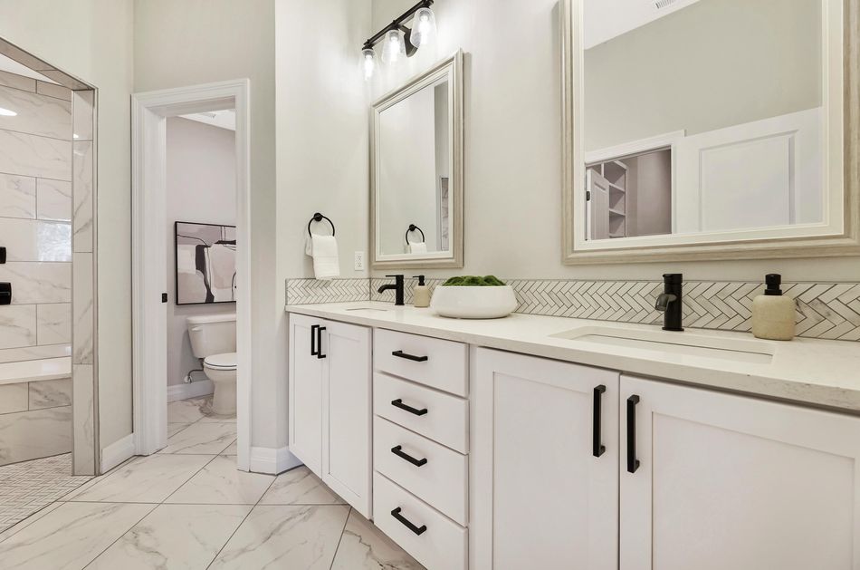 Primary bathroom at 4658 W Emerald Bay Court with a long double vanity, framed mirrors and a herringbone tile backsplash – Wichita, KS