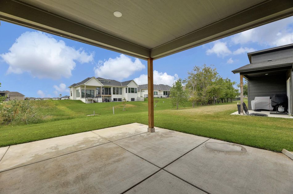Covered rear patio at 4658 W Emerald Bay Court looking across the back lawn towards neighbouring homes – Wichita, KS