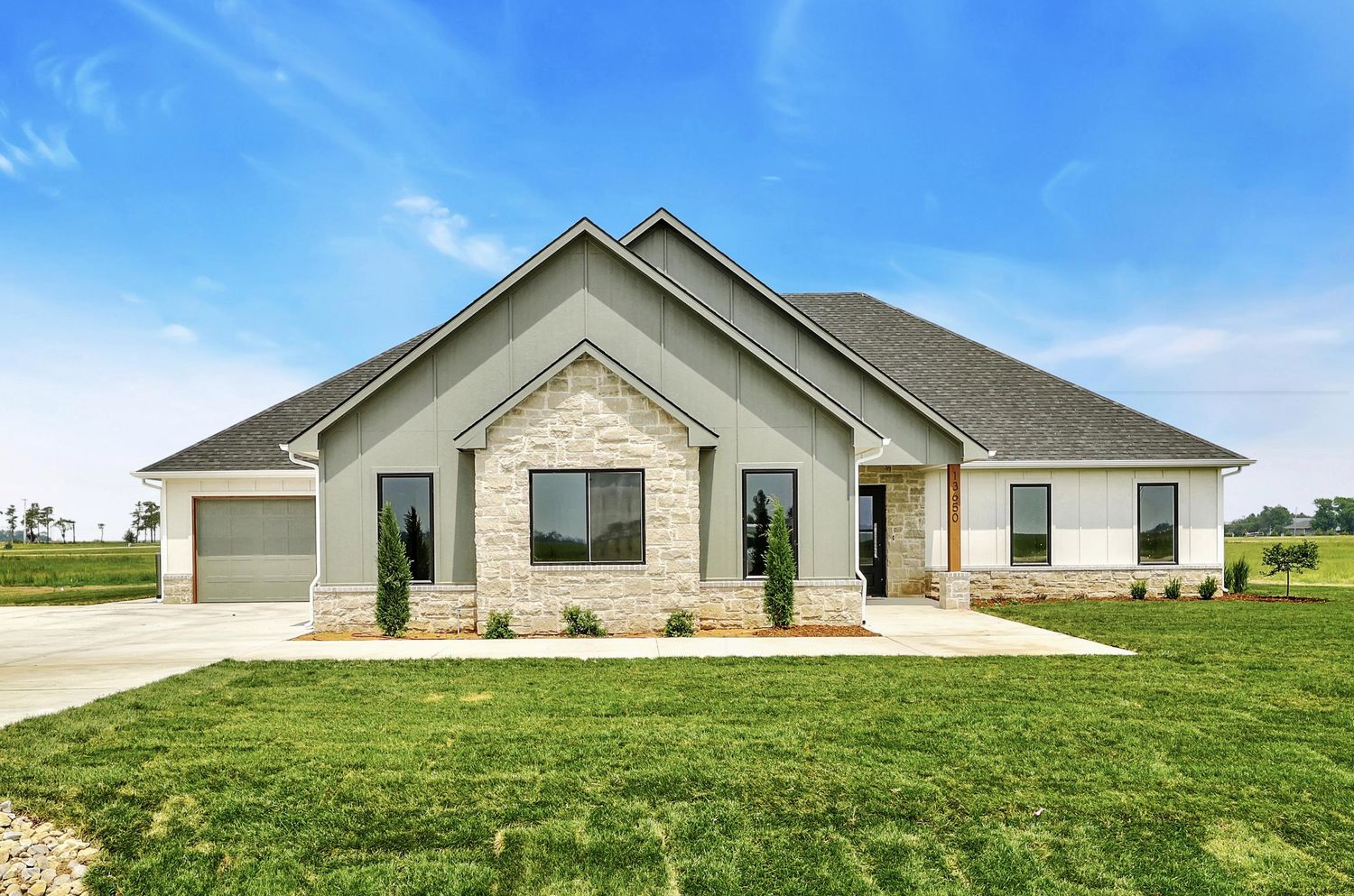 Front elevation of 13650 W Homestead Drive — a sage board-and-batten ranch with a full-height limestone gable on an acre lot – Colwich, KS