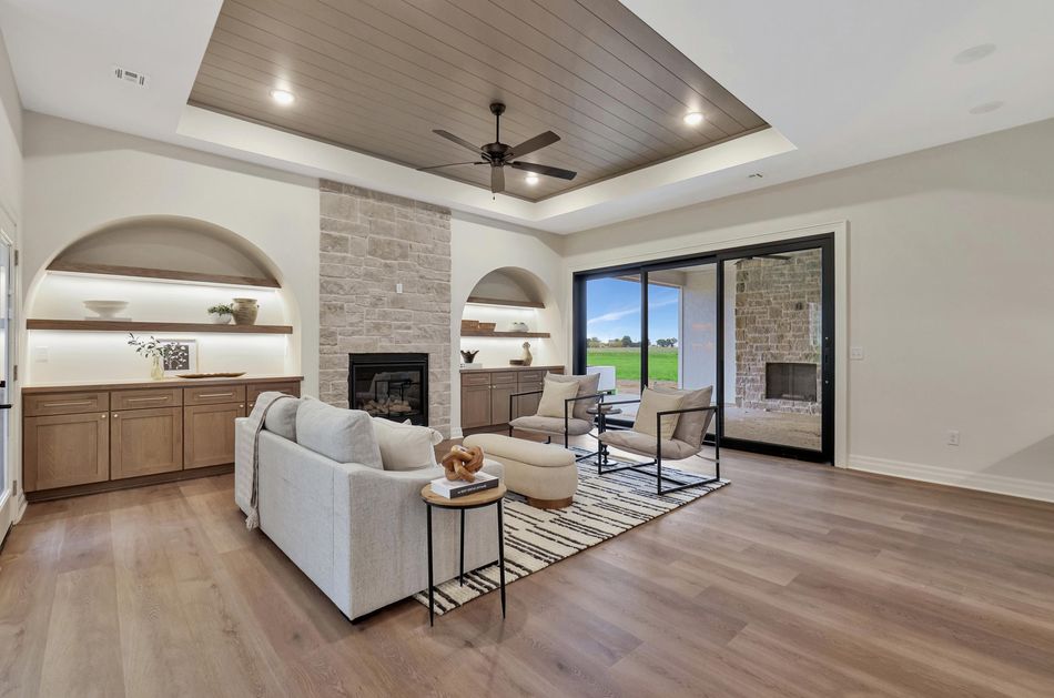 Great room with a limestone fireplace between arched lit alcoves under a planked tray ceiling at 13650 W Homestead Drive – Colwich, KS