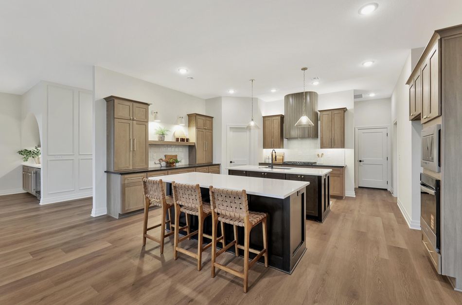 Kitchen at 13650 W Homestead Drive with stained oak cabinetry, a dark island with woven bar stools and a fluted range hood – Colwich, KS