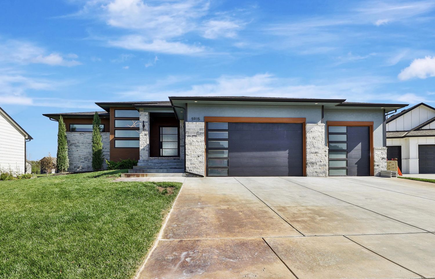 Front elevation of 5915 W Kollmeyer Court — a flat-roofed contemporary home in charcoal siding and limestone with a glazed garage door – Wichita, KS