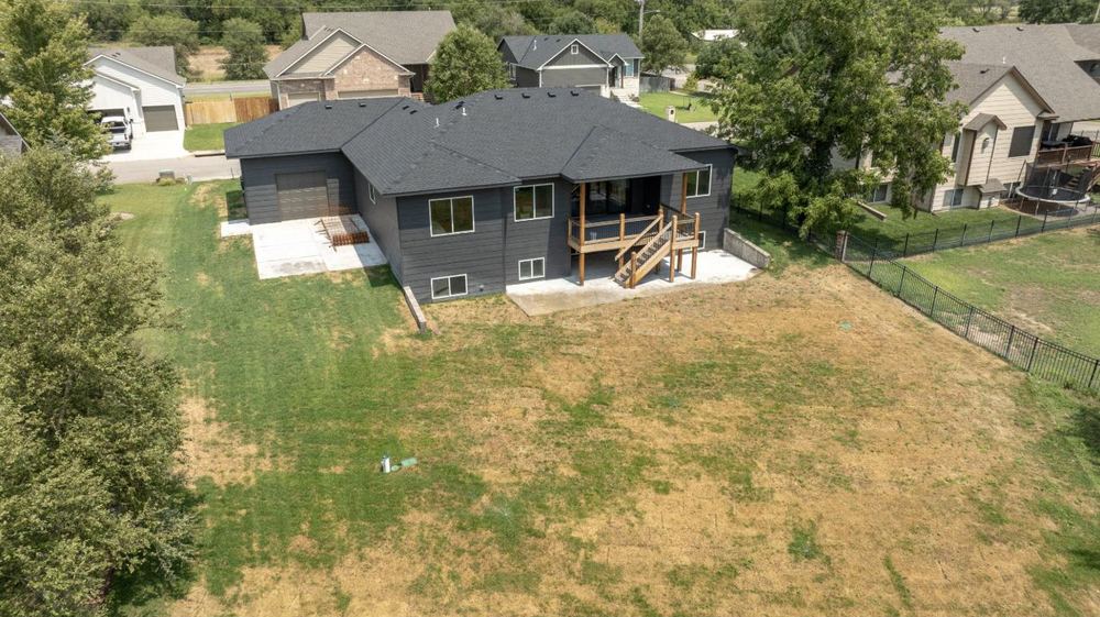 Drone view of the rear elevation of 3117 Sunflower Drive showing the walkout, the deck and stairs down to the lawn – Derby, KS