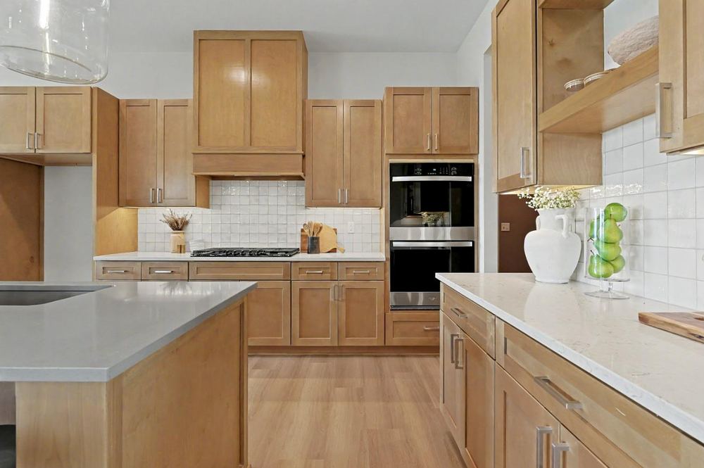 Kitchen range wall at 3117 Sunflower Drive with stained maple cabinetry, a cabinet hood surround, white tile backsplash and double wall ovens – Derby, KS