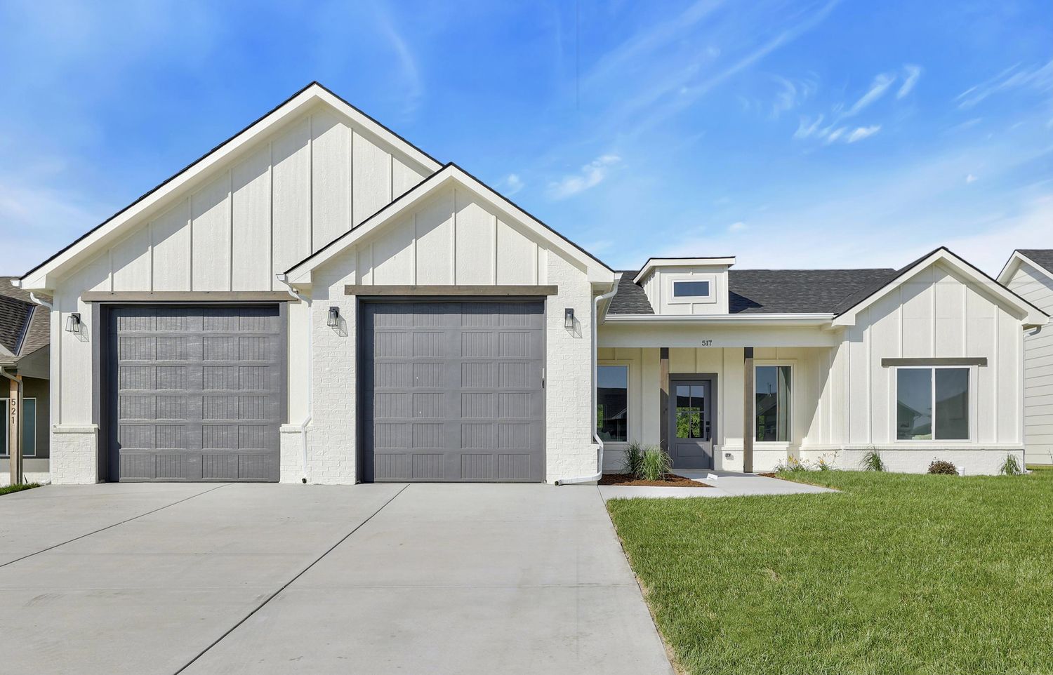 Front elevation of 517 S Sweetwater Road — twin board-and-batten gables in off-white with charcoal garage doors and an entry dormer – Maize, KS